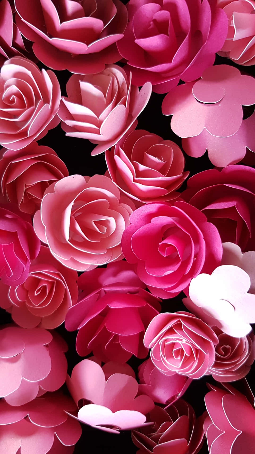 Close-up of handmade paper roses in shades of pink against black background.