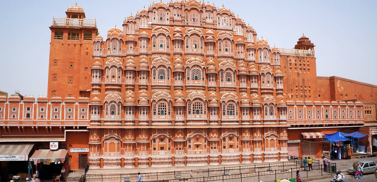 A historic Indian palace with ornate carvings and balconies stands tall above a busy street.